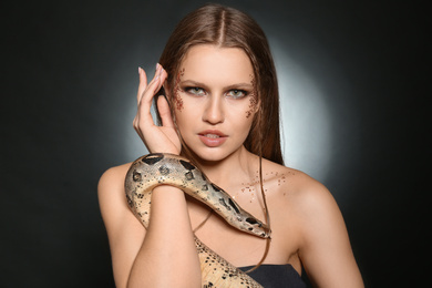 Beautiful woman with boa constrictor on dark background