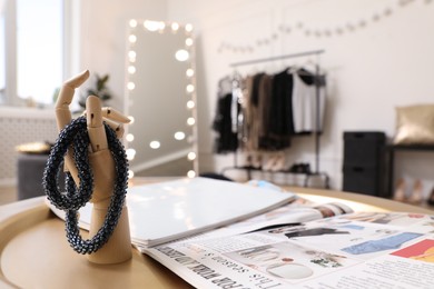 Photo of Wooden mannequin hand with necklace and magazines on golden table. Dressing room interior