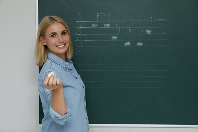 Teacher near green chalkboard with music notes in classroom