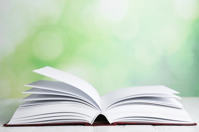 Open book on white wooden table against blurred green background. Space for text