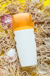 Bottle of suntan cream, seashells and net on yellow background, flat lay