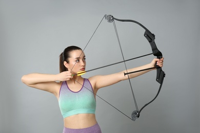 Young woman practicing archery on light grey background