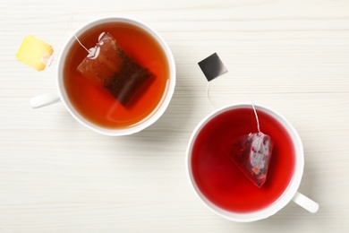 Photo of Different tea bags in cups of hot water on white wooden table, flat lay