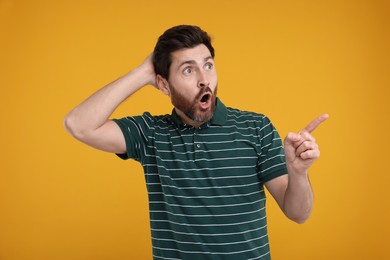 Surprised man pointing at something on yellow background