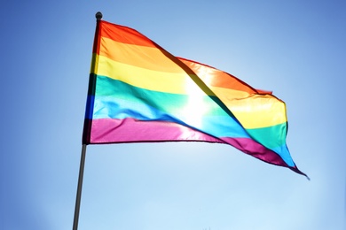 Photo of Rainbow LGBT flag fluttering on blue sky background. Gay rights movement