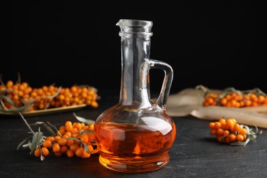 Photo of Ripe sea buckthorn and jug of essential oil on black table
