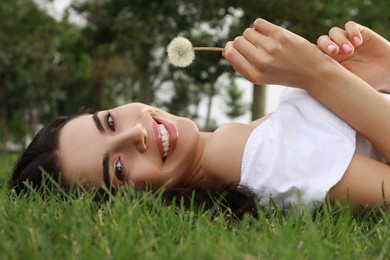 Photo of Beautiful young woman with dandelion lying on green grass in park. Allergy free concept