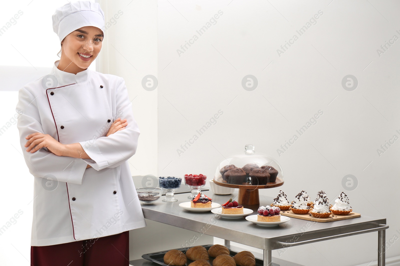 Photo of Female chef near table with different pastries in kitchen