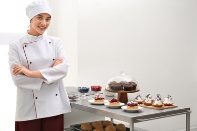 Photo of Female chef near table with different pastries in kitchen