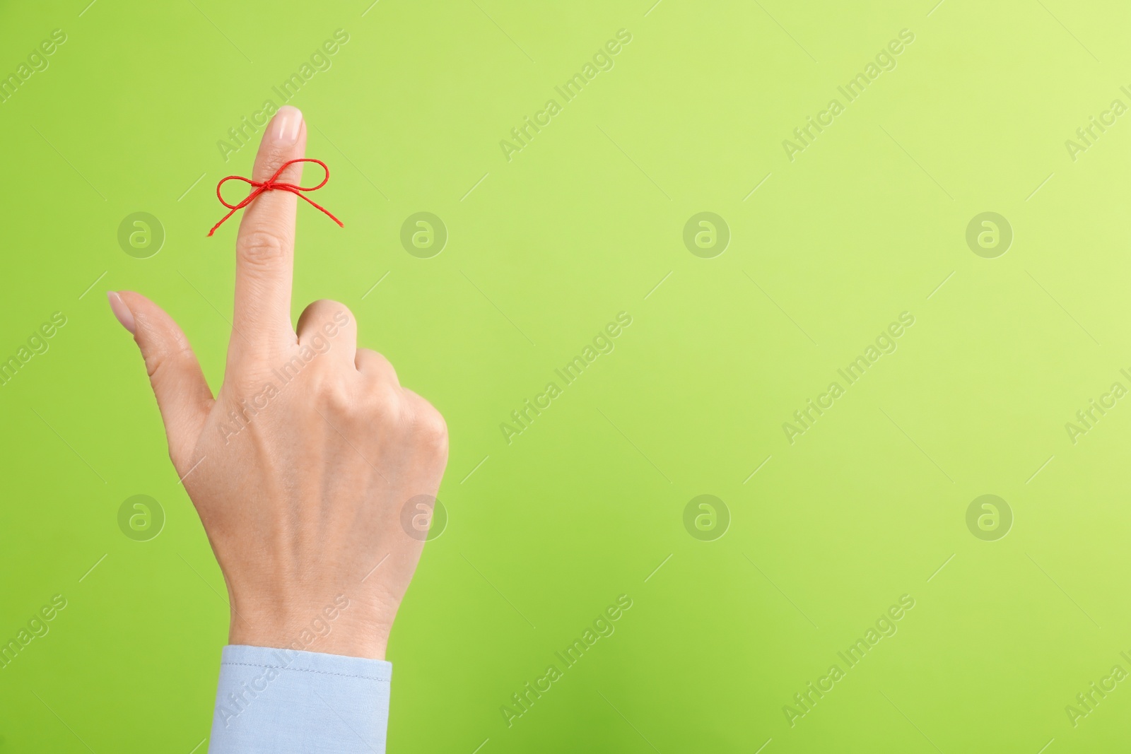 Photo of Woman showing index finger with tied red bow as reminder on light green background, closeup. Space for text