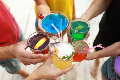 Friends clinking glasses with fresh summer cocktails outdoors, closeup