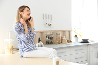 Photo of Young woman talking on phone in kitchen