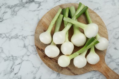 Photo of Wooden board with green spring onions on white marble table, top view. Space for text