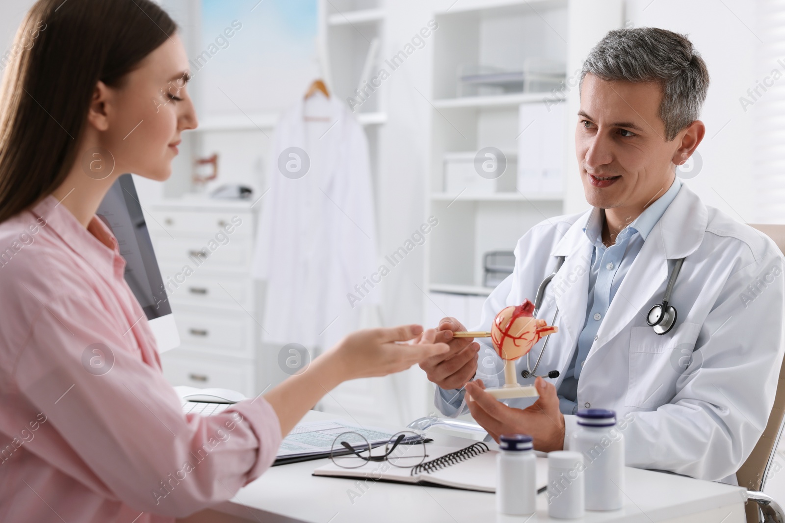 Photo of Gastroenterologist with human stomach model consulting patient at table in clinic