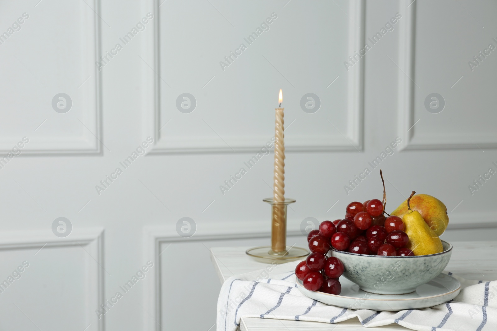 Photo of Fresh ripe fruits and burning candle on table indoors. Space for text