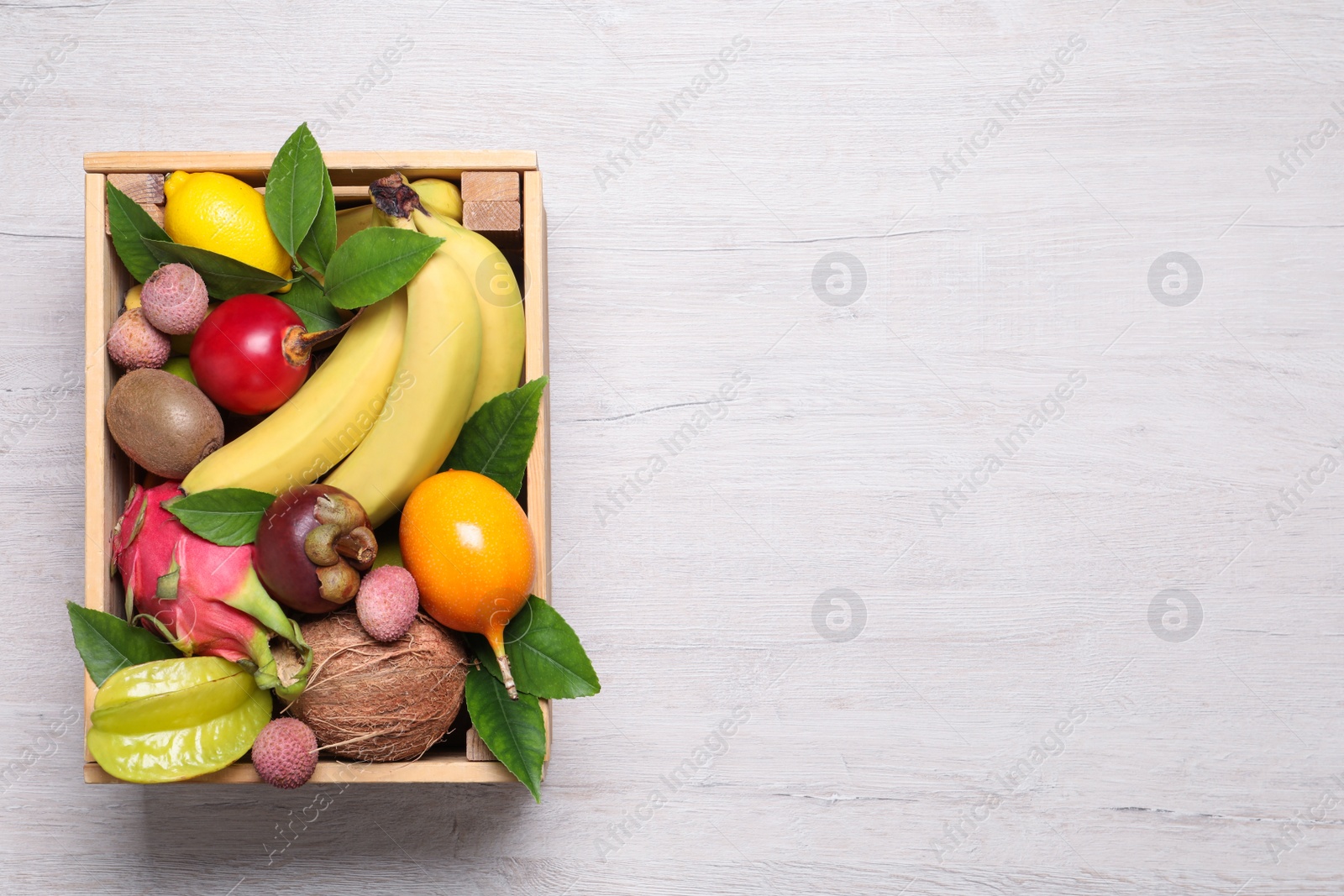 Photo of Crate with different exotic fruits on white wooden table, top view. Space for text