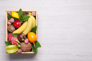 Photo of Crate with different exotic fruits on white wooden table, top view. Space for text