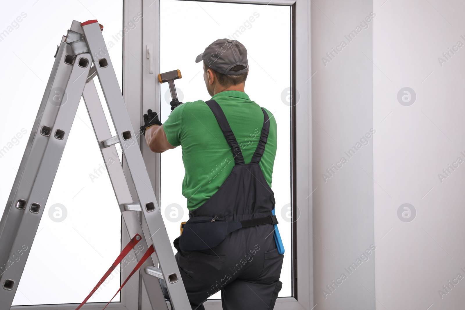 Photo of Worker using hammer for double glazing window installation indoors, back view