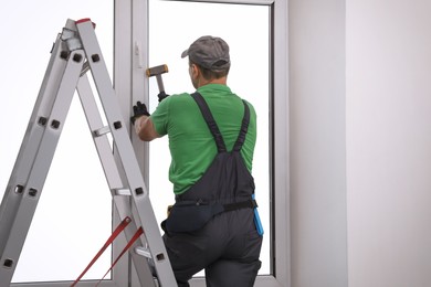 Photo of Worker using hammer for double glazing window installation indoors, back view