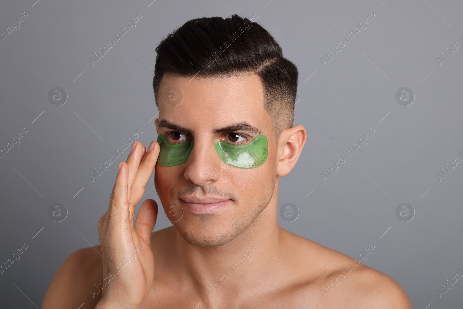 Photo of Man applying green under eye patch on grey background