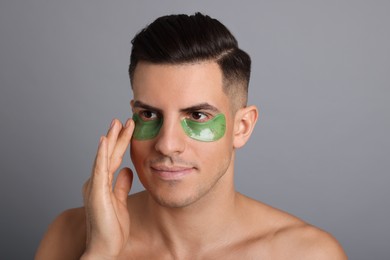 Man applying green under eye patch on grey background