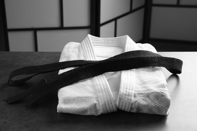 Photo of Martial arts uniform with black belt on grey stone table indoors