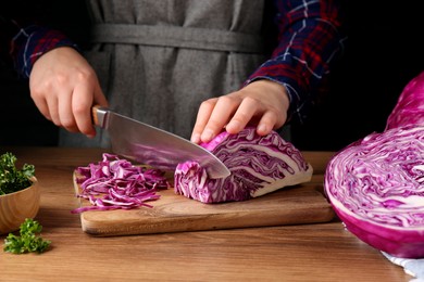 Photo of Woman cutting fresh red cabbage at wooden table, closeup