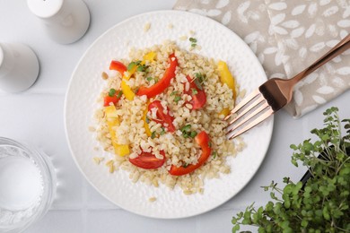 Photo of Plate of cooked bulgur with vegetables on white tiled table, flat lay