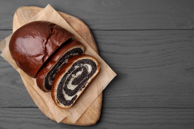 Cut poppy seed roll on grey wooden table, top view with space for text. Tasty cake