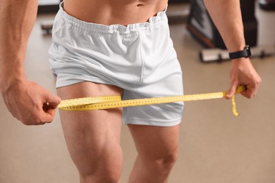Photo of Athletic man measuring thigh with tape in gym, closeup