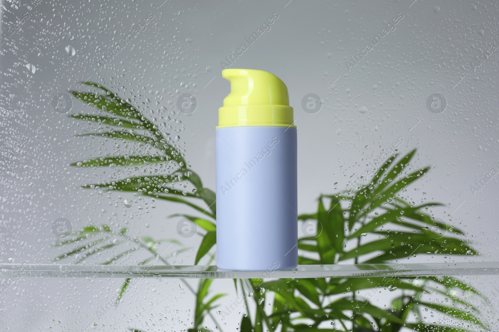 Photo of Bottle with moisturizing cream and palm leaves on light background, view through wet glass