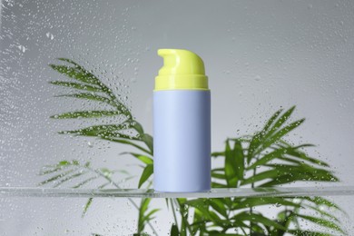 Bottle with moisturizing cream and palm leaves on light background, view through wet glass