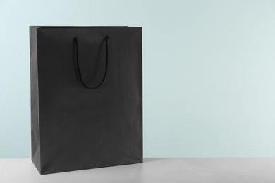 Photo of Black shopping paper bag on table against light background. Space for text