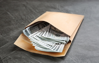 Photo of Envelope with dollar bills on grey stone table. Bribe concept