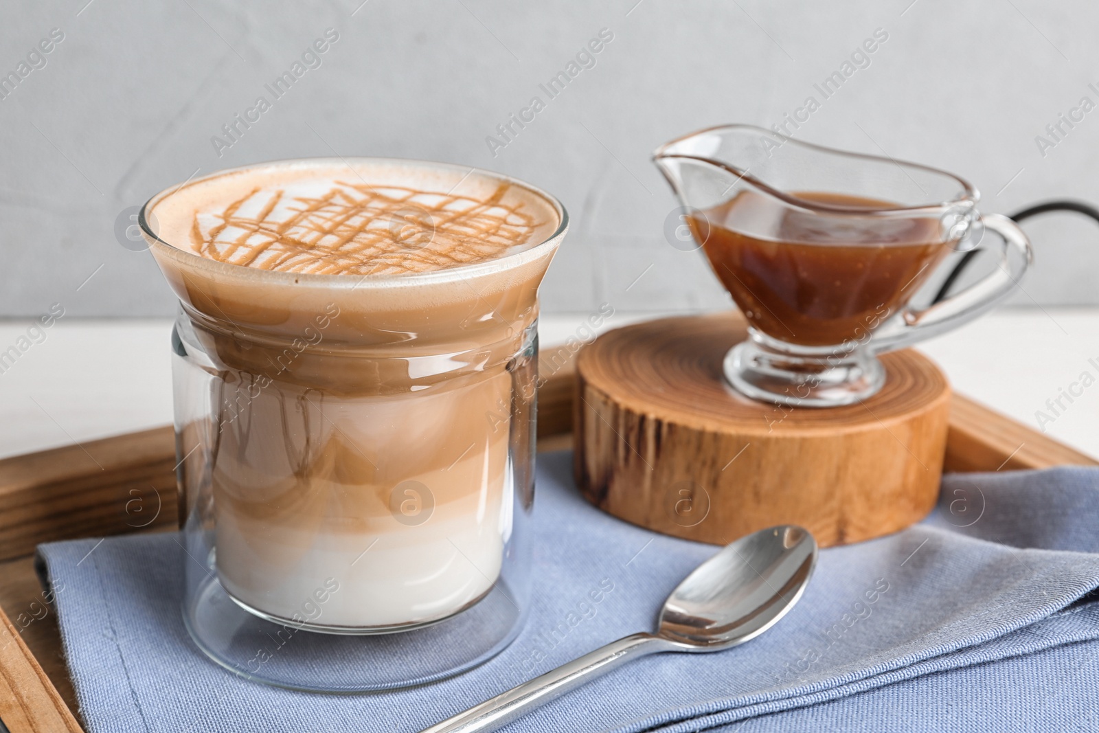 Photo of Glass of caramel macchiato and gravy boat with sauce on table