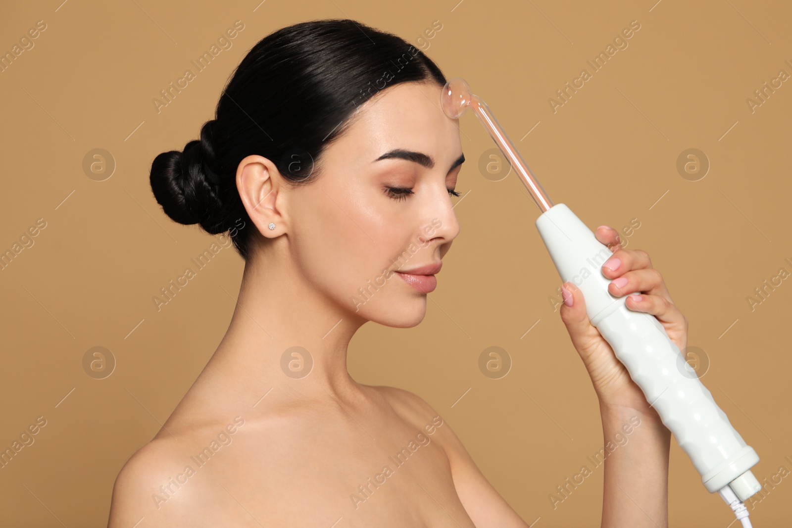 Photo of Woman using high frequency darsonval device on beige background