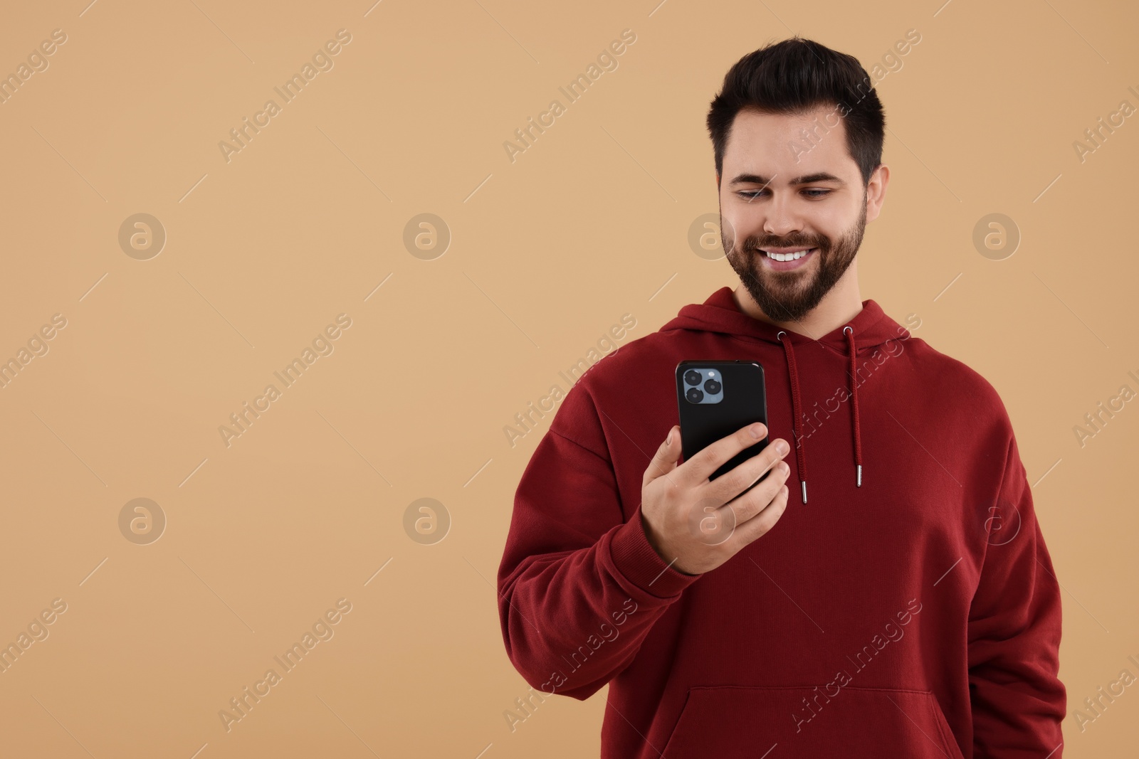 Photo of Happy young man using smartphone on beige background, space for text