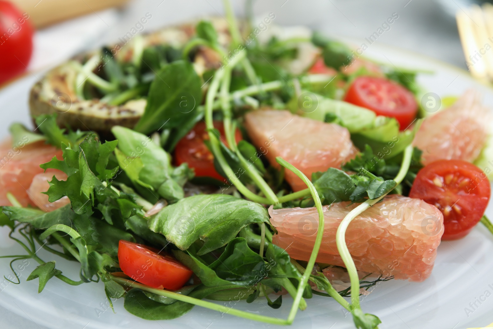 Photo of Delicious pomelo salad with tomatoes and microgreens on plate, closeup