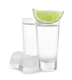 Shot glasses of vodka with lime slice and ice on white background