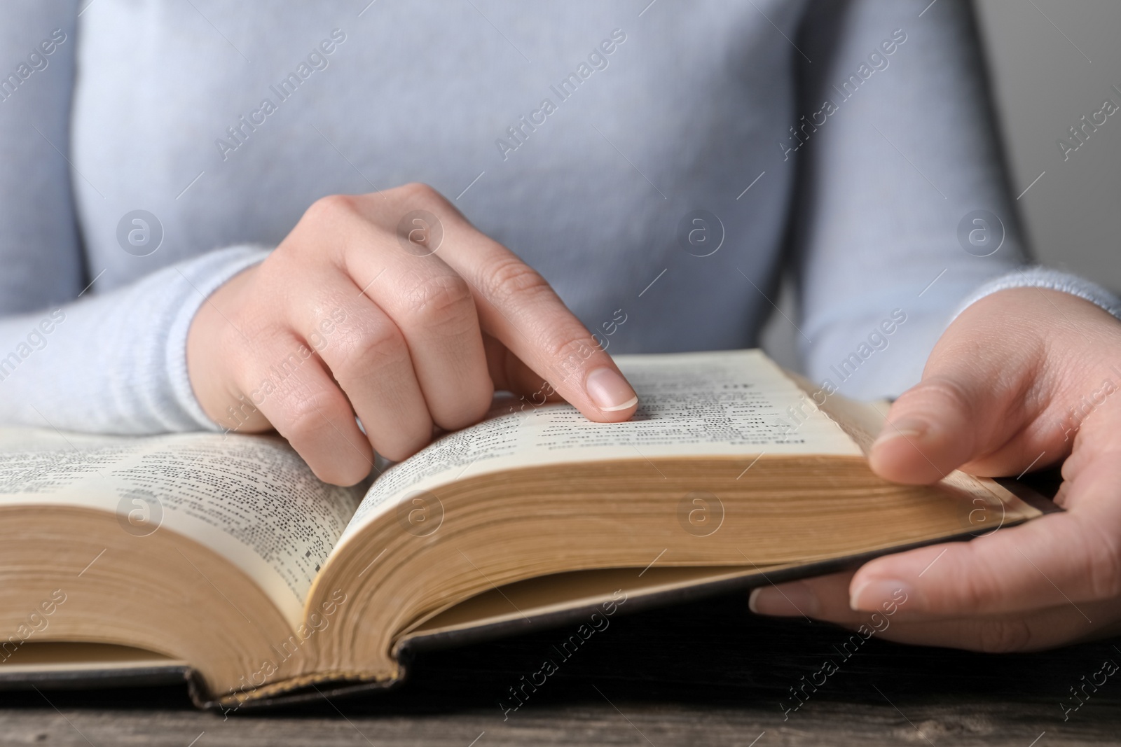 Photo of Woman reading Bible at wooden table, closeup