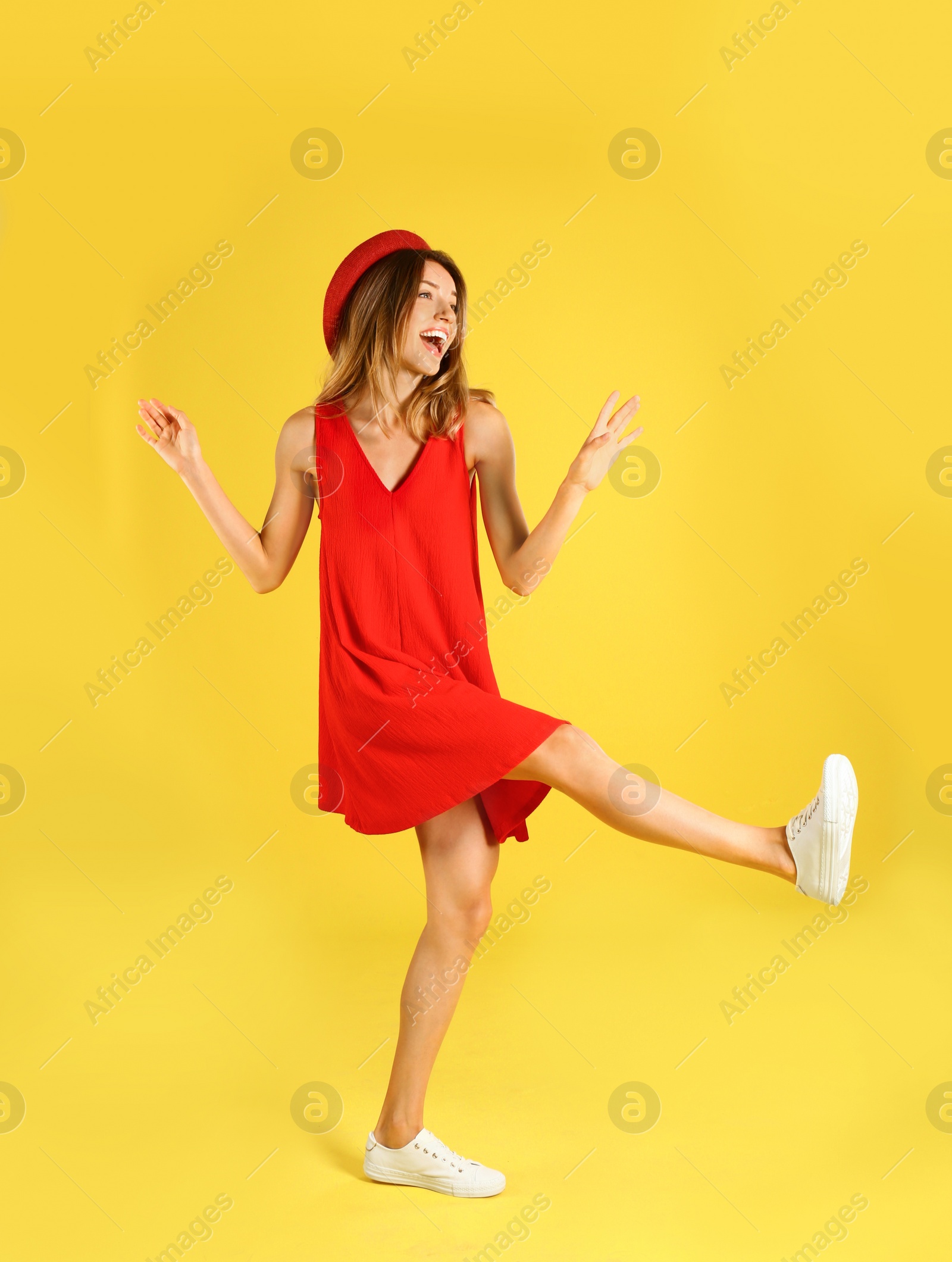 Photo of Beautiful young woman in red dress dancing on yellow background