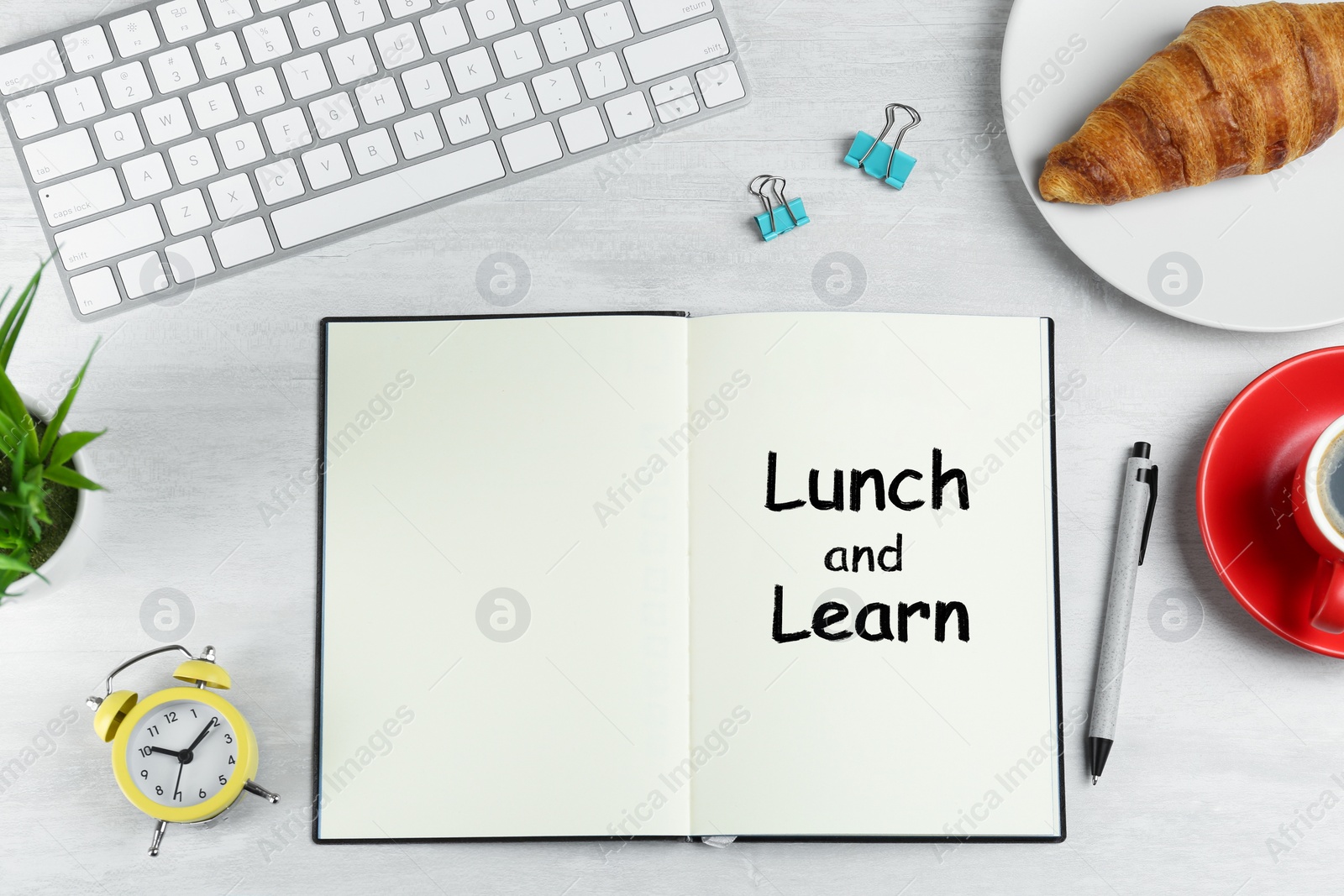 Image of Lunch and Learn concept. Notebook, coffee, alarm clock, computer keyboard, croissant and stationery on white table, flat lay