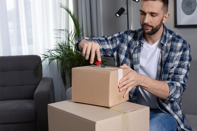 Photo of Man using utility knife to open parcel at home