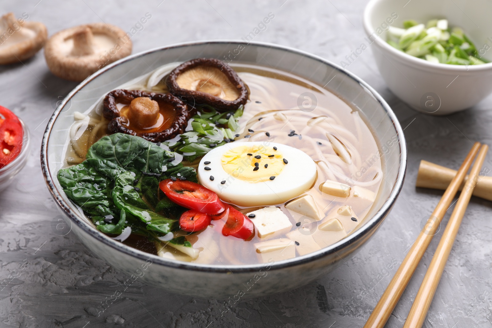 Photo of Delicious vegetarian ramen served on grey table, closeup. Noodle soup