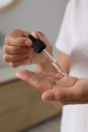 Woman applying cosmetic serum onto her hand on blurred background, closeup