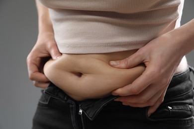 Photo of Woman touching belly fat on grey background, closeup. Overweight problem