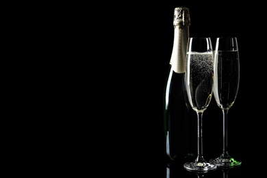 Bottle and glasses of champagne on black background, space for text