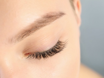 Photo of Young woman with beautiful long eyelashes on gray background, closeup. Extension procedure