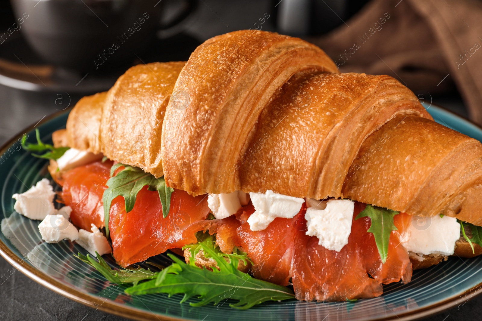 Photo of Tasty croissant sandwich with red fish on grey table, closeup