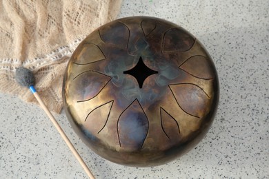 Photo of Steel tongue drum and soft mallet on grey table, above view. Percussion musical instrument